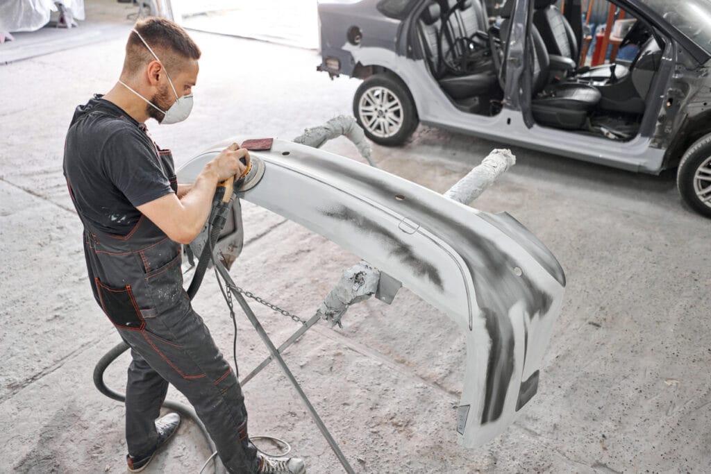 The mechanic works with a grinding tool. Sanding of car elements. Garage painting car service. Repairing car section after the accident.